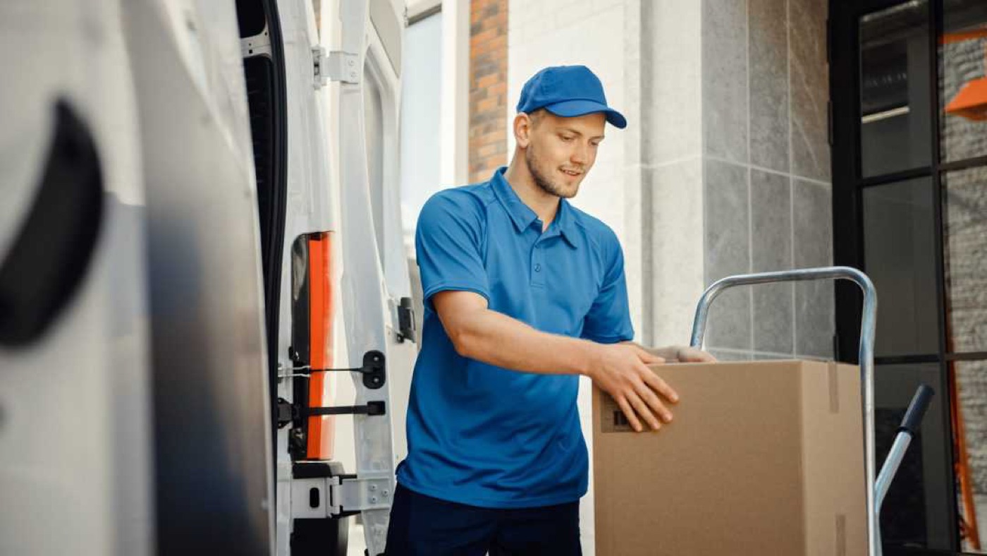 A driver loading boxes into a van with a sack truck